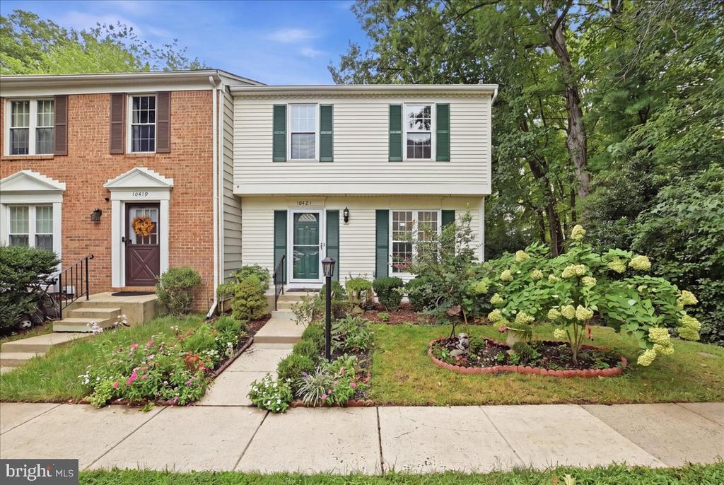 Two-story townhouse with green shutters, a front walkway, and landscaped flower beds.