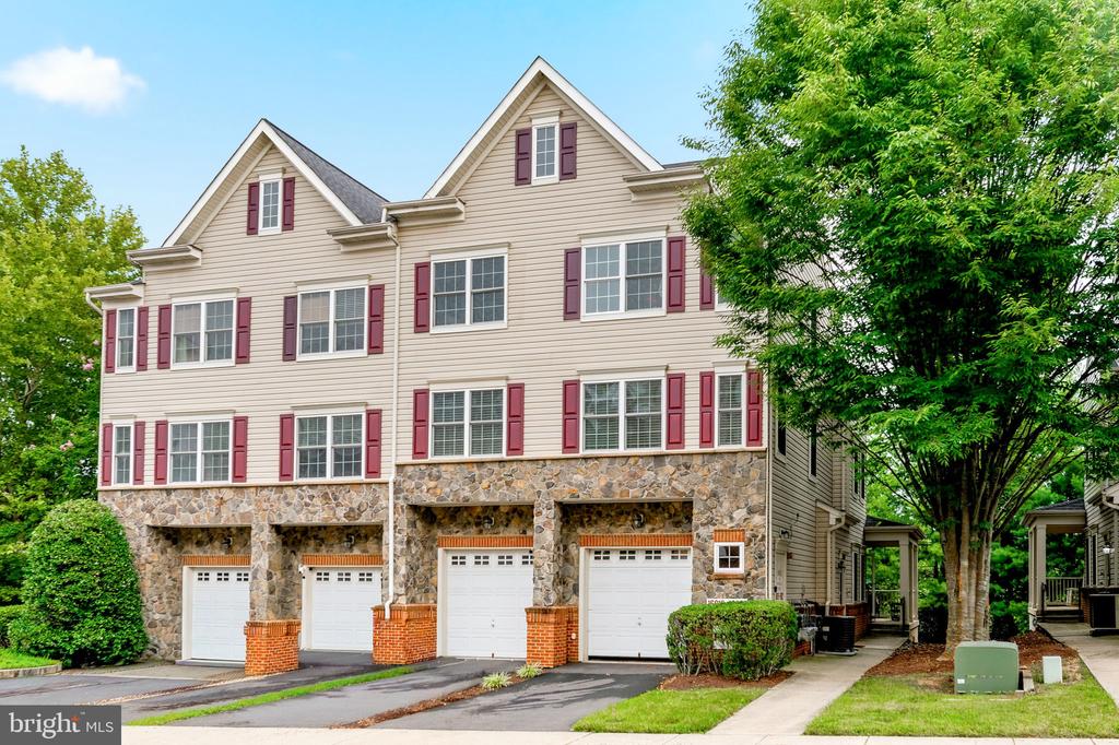 Attached townhomes with stone garage level, red shutters, and mature trees.