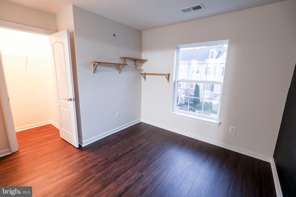 Vacant bedroom with dark wood floors, built-in closet shelves, and a window overlooking neighboring homes.