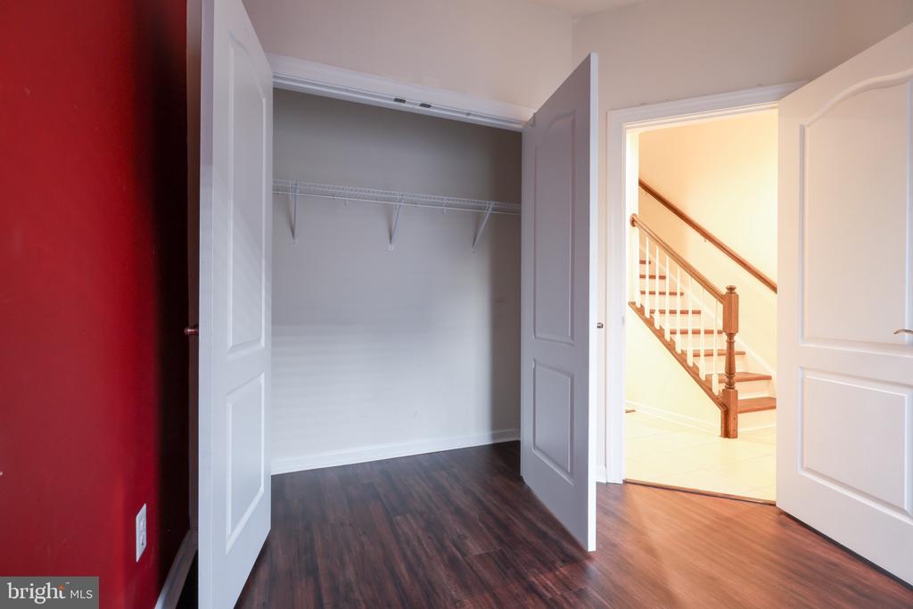 Empty bedroom with an open closet, dark wood floors, red accent wall, and staircase beyond.