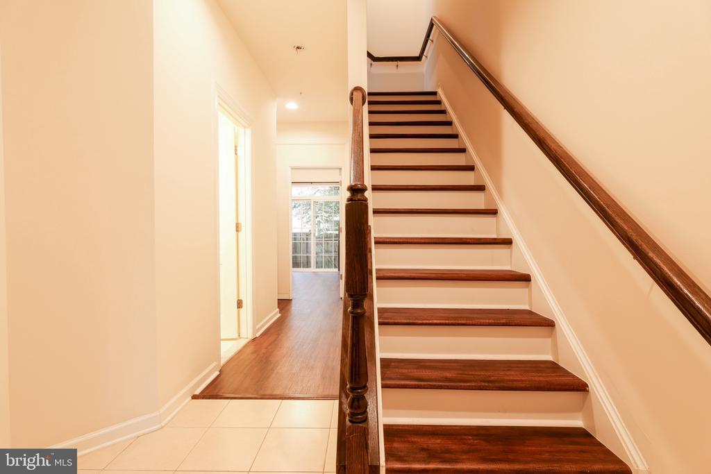 Foyer staircase with dark wood treads and handrails beside a wood-floored hallway.