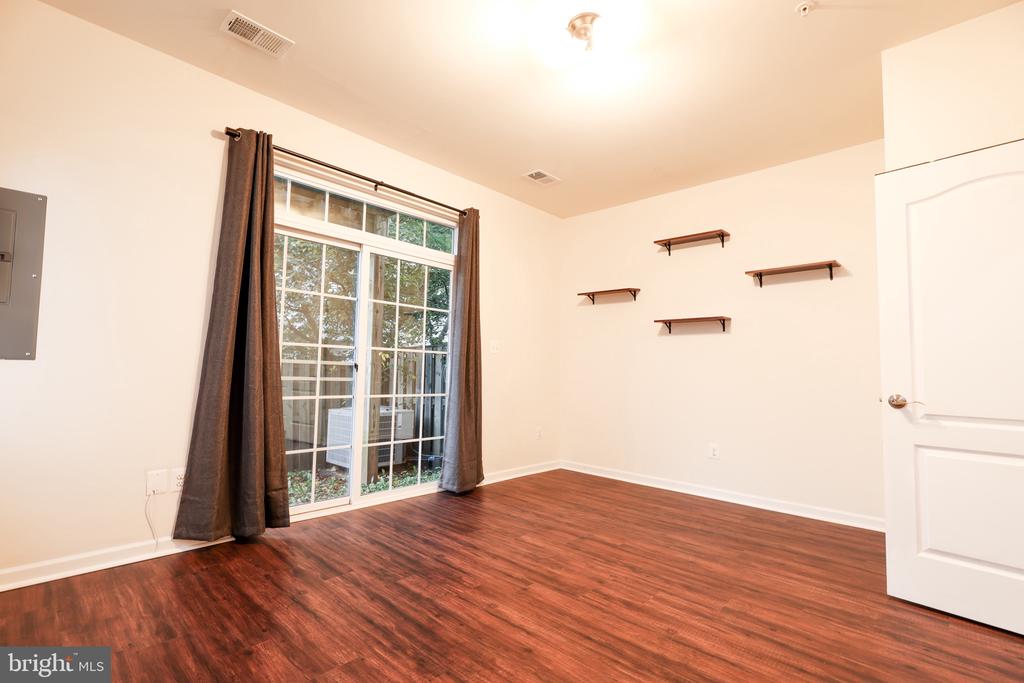 Empty room with wood flooring, sliding glass doors, dark curtains, and floating shelves.