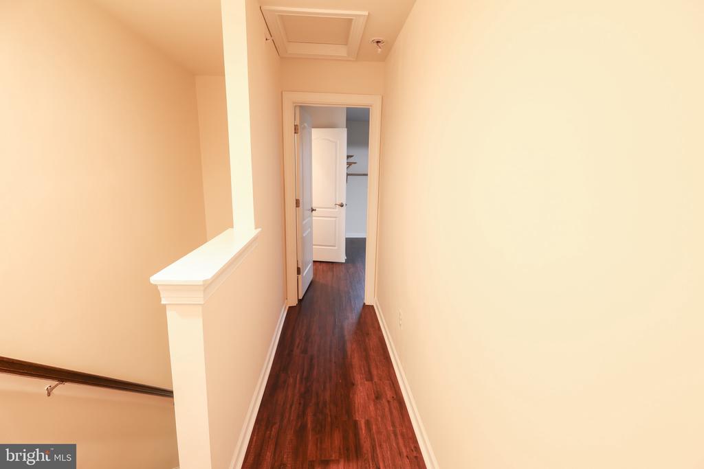 Narrow hallway with dark hardwood floors and an open doorway at the far end.