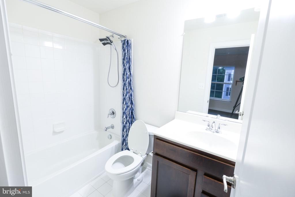 Bathroom with a white tiled tub, blue patterned shower curtain, and dark wood vanity.