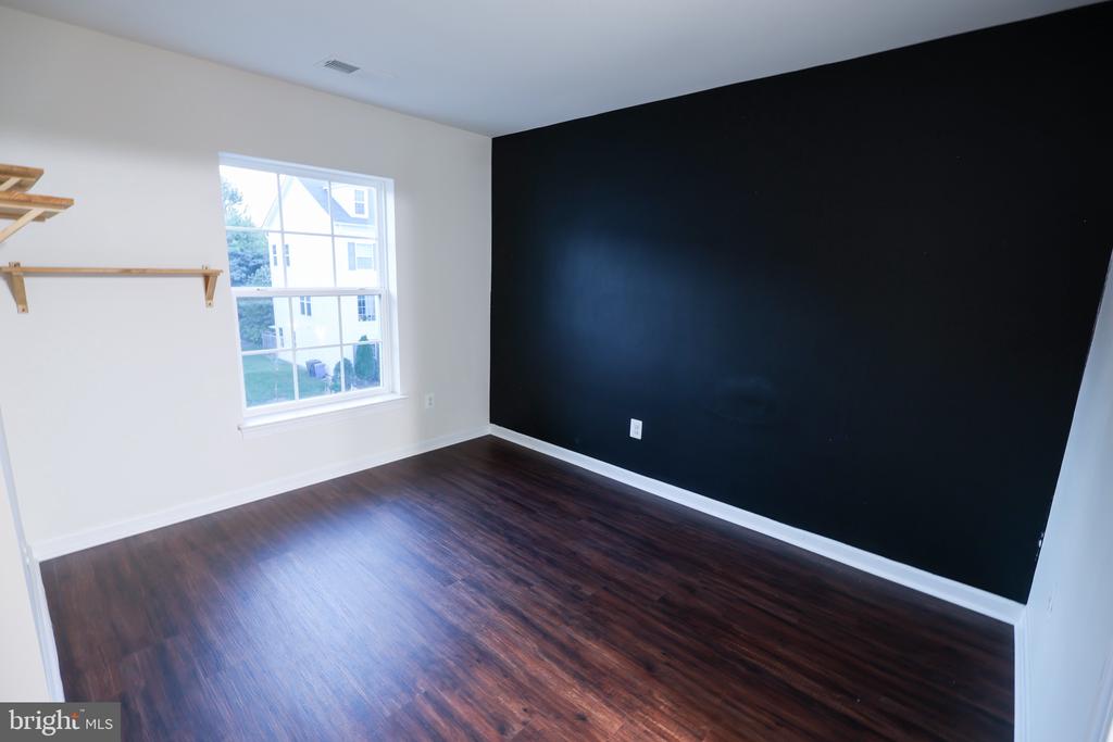 Empty room with dark wood floors, a black accent wall, and a large window.
