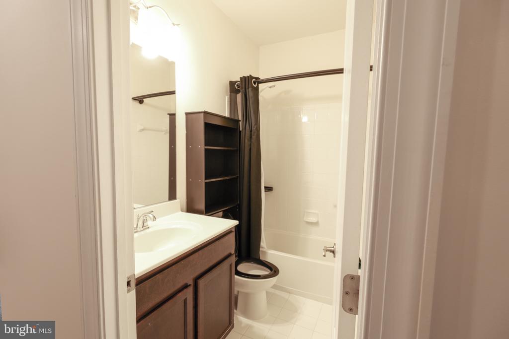 Bathroom with dark wood vanity, toilet, and white tub behind a dark shower curtain.