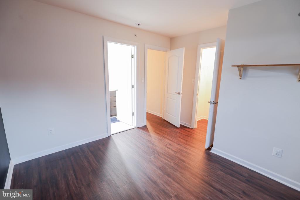 Vacant room with dark wood-look flooring, a wall shelf, and multiple open doorways.