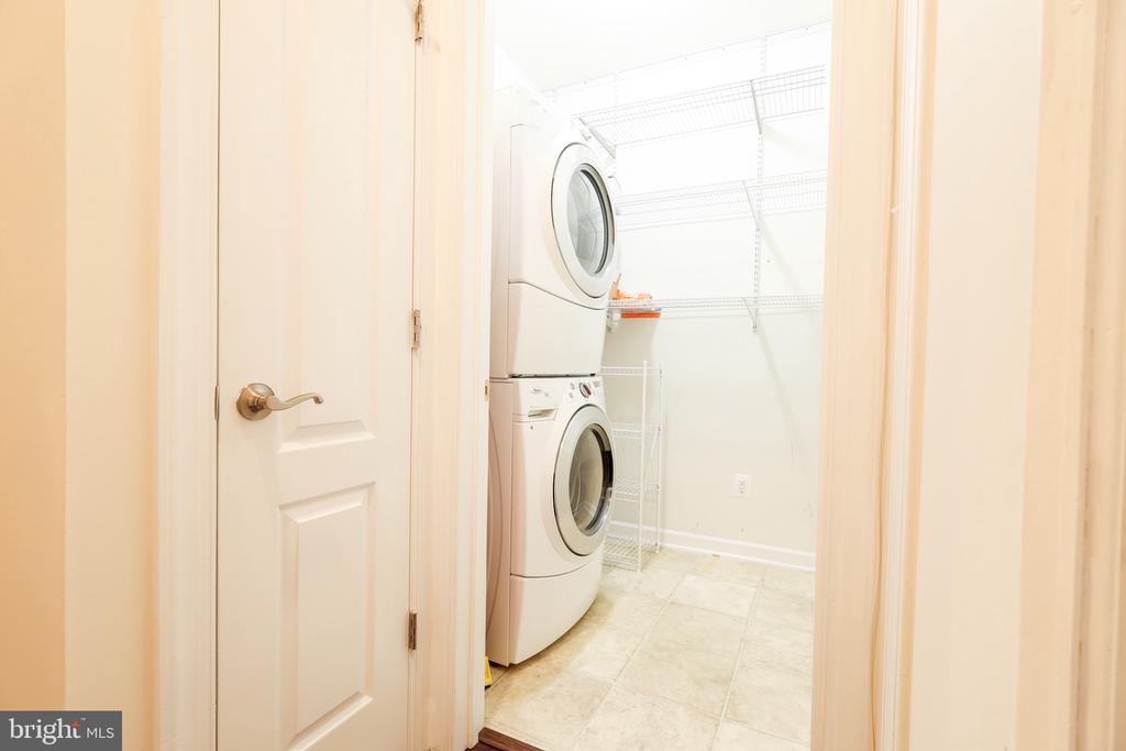 Laundry room with stacked front-loading washer and dryer beneath wire shelving.