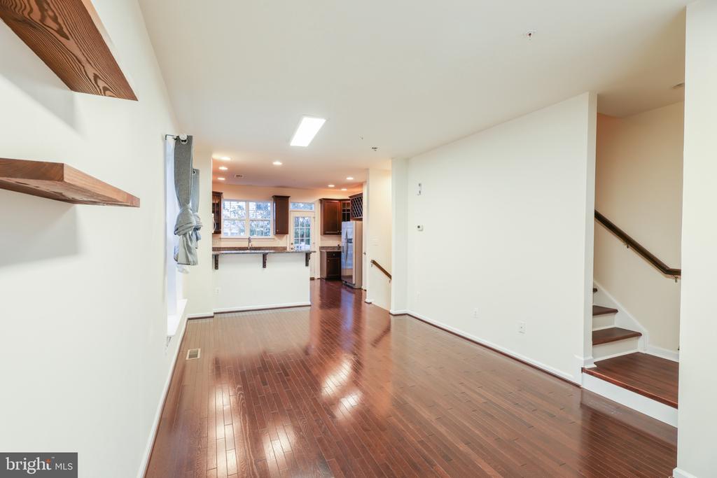 Unfurnished living area with glossy hardwood floors, floating wood shelves, and an open kitchen beyond.
