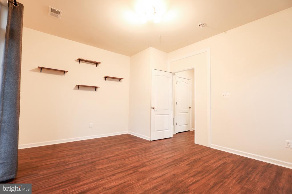 Unfurnished room with reddish-brown wood flooring, wall shelves, and an open doorway.