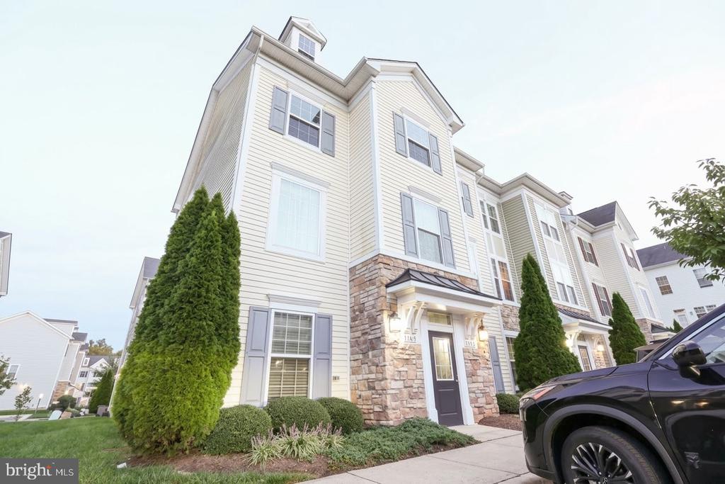 Cream townhouse with stone facade accents and gray shutters, viewed from the sidewalk.