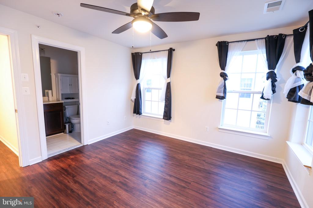 Vacant bedroom with dark wood floors, a ceiling fan, and curtained windows.