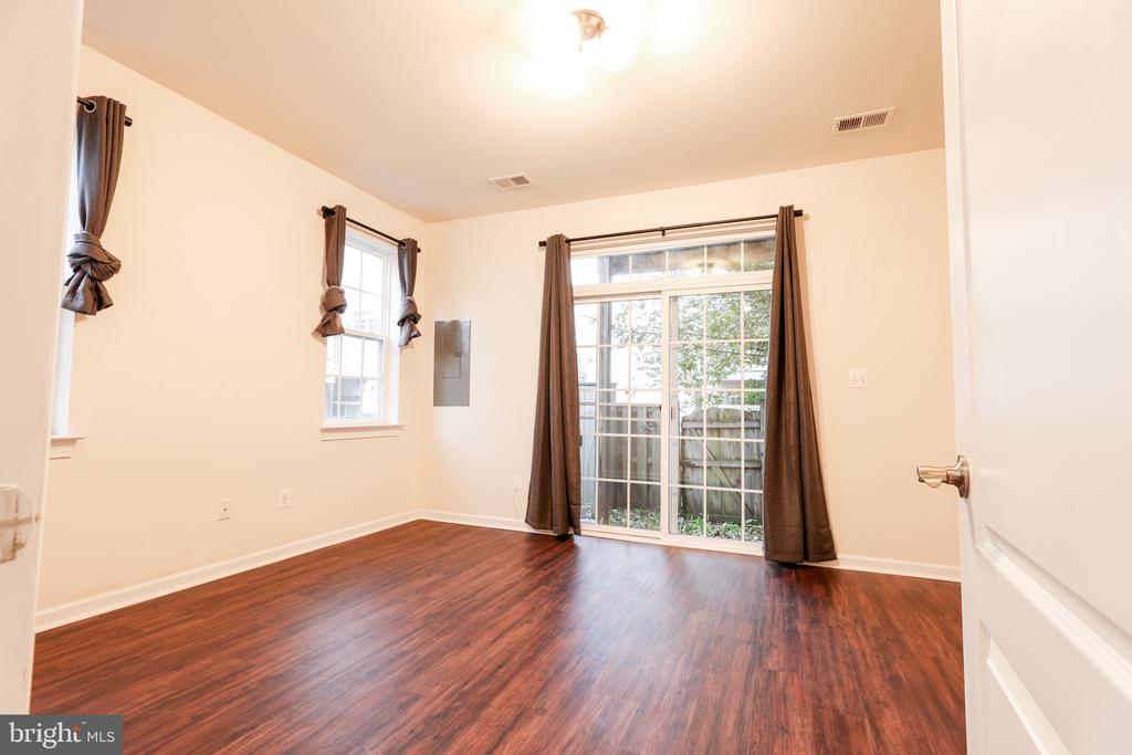 Empty room with wood-look flooring, curtained windows, and a sliding glass door to a fenced area.