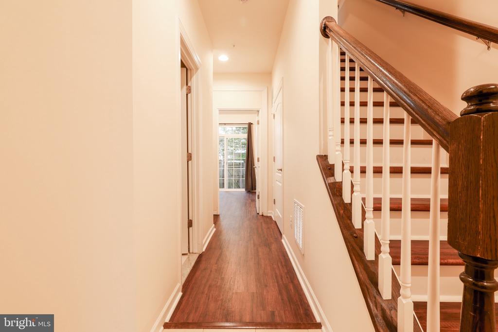 Hallway with wood flooring beside a staircase with dark wood rails and white balusters.