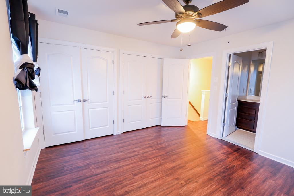 Empty bedroom with hardwood floors, paneled closet doors, and a ceiling fan.