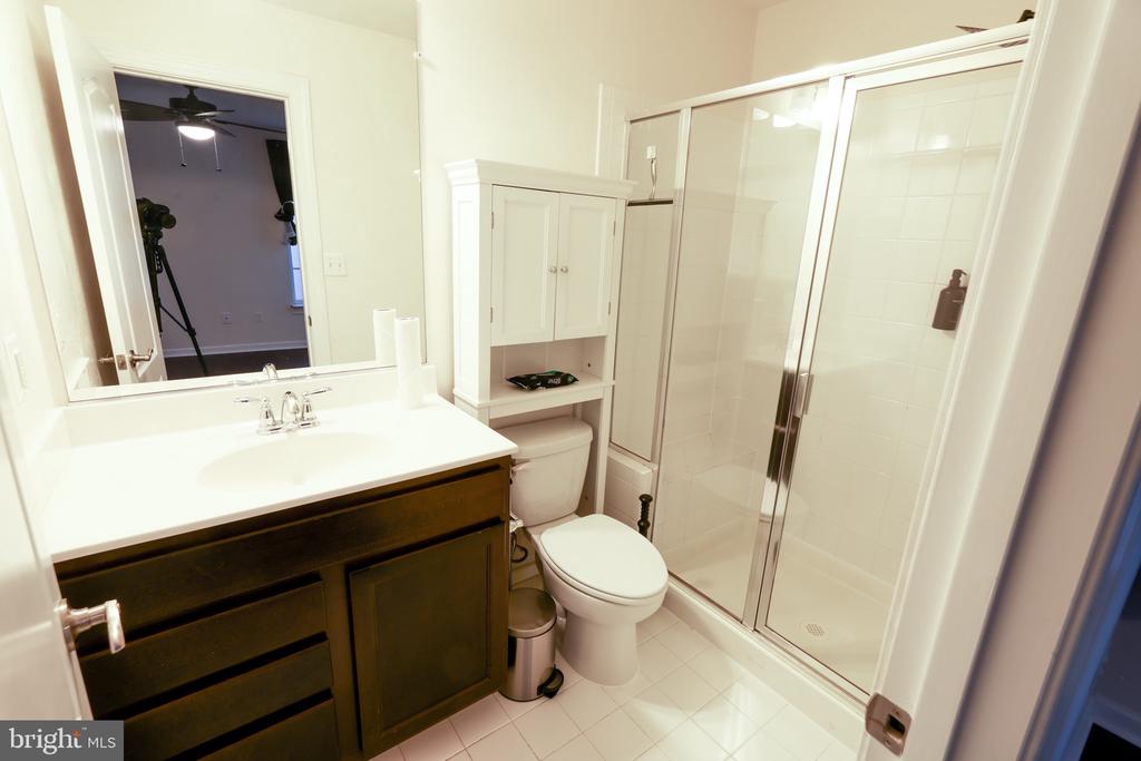 Bathroom with a dark wood vanity, built-in cabinet above the toilet, and glass-enclosed shower.