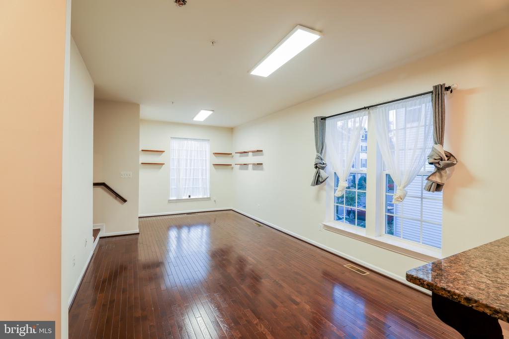 Empty living room with polished hardwood floors, large curtained windows, and floating shelves.