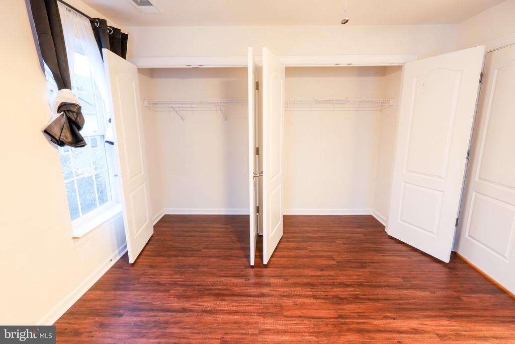 Empty dressing area with two open closets, wire shelving, dark wood floors, and a curtained window.