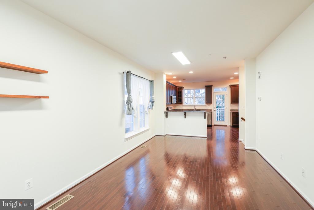 Empty open living and dining area with hardwood floors, tall windows, and kitchen beyond.
