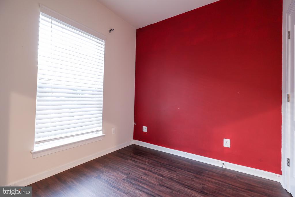 Empty room with dark wood floors, a red accent wall, and a window with white blinds.