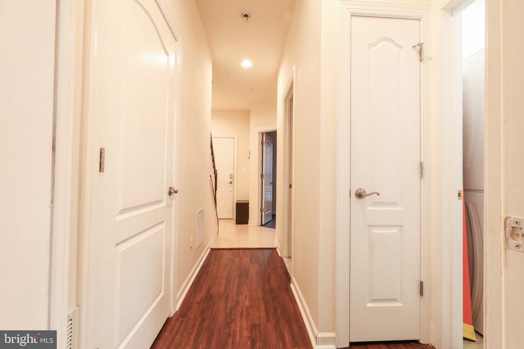 Interior hallway with dark wood flooring, white doors, and a tiled entry.