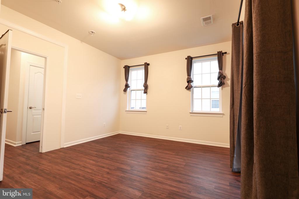 Empty room with reddish-brown flooring, two curtained windows, and a doorway.