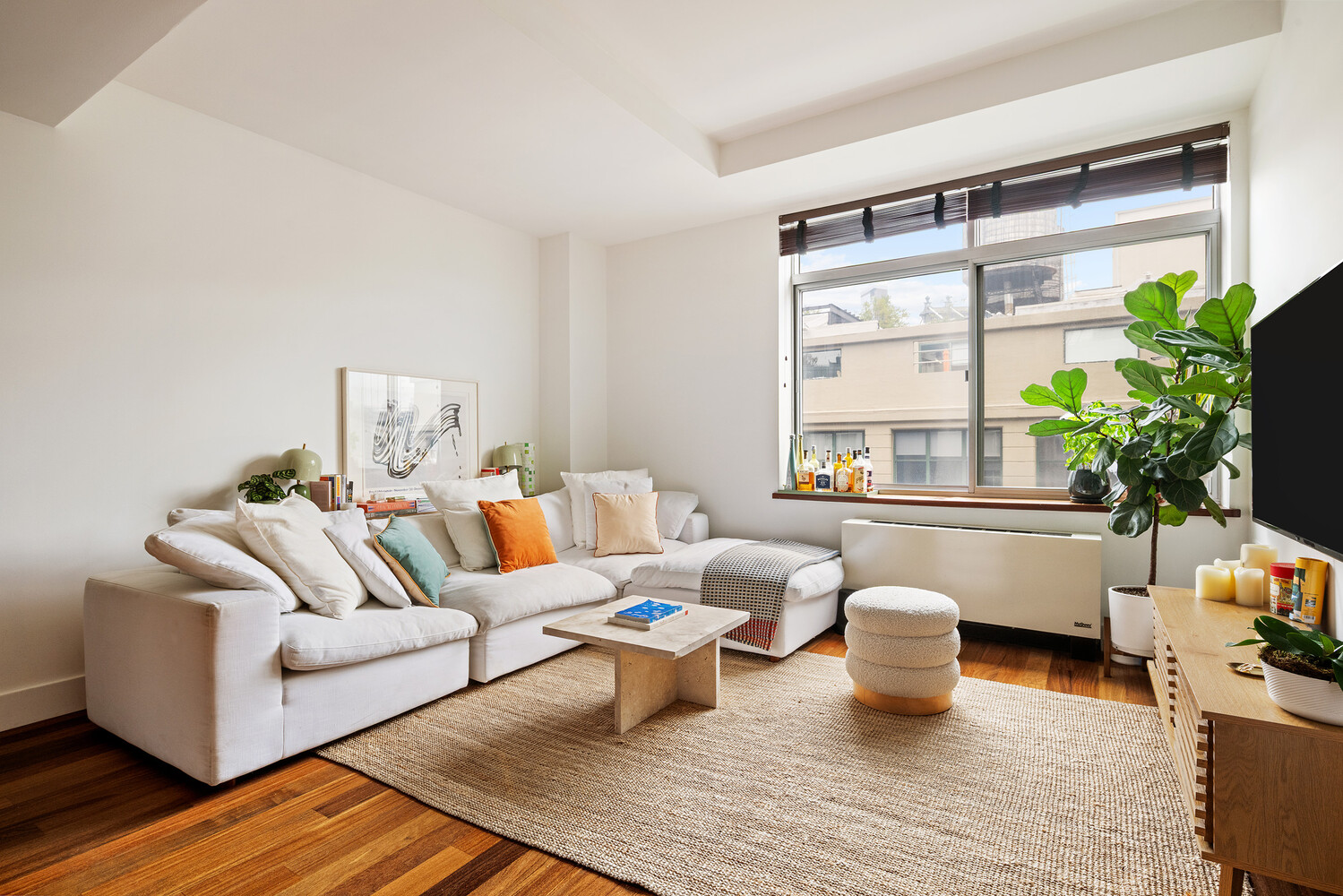 Living room with a white sectional sofa, warm wood floors, and a large sunlit window.