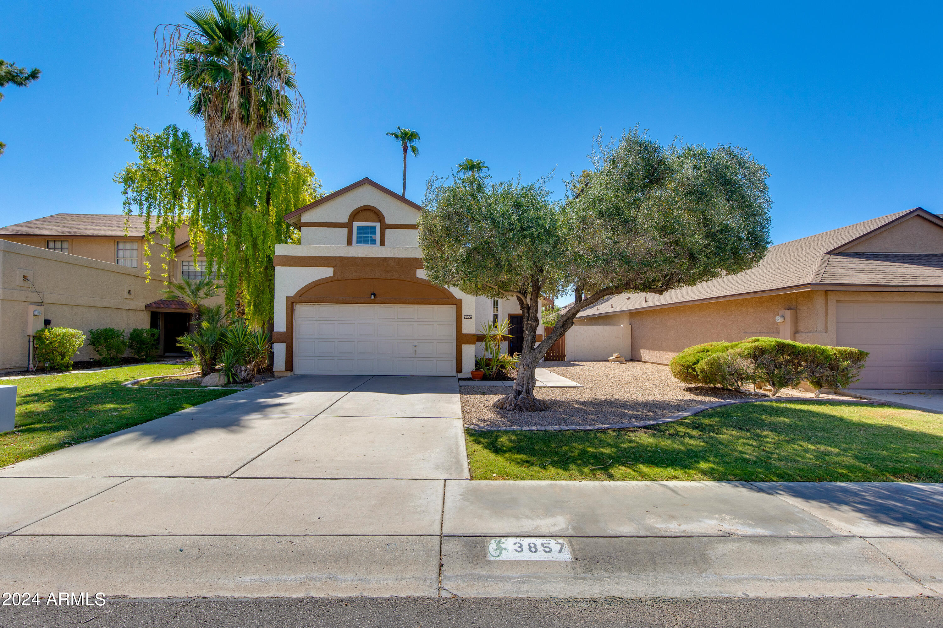 Two-story stucco home with a double garage, broad driveway, and mature palm trees.