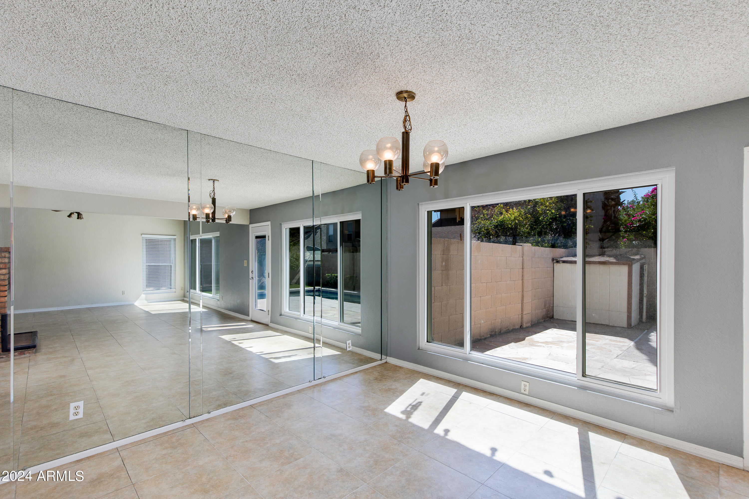 Vacant living room with a mirrored wall, tile floors, and sliding glass doors to a patio.