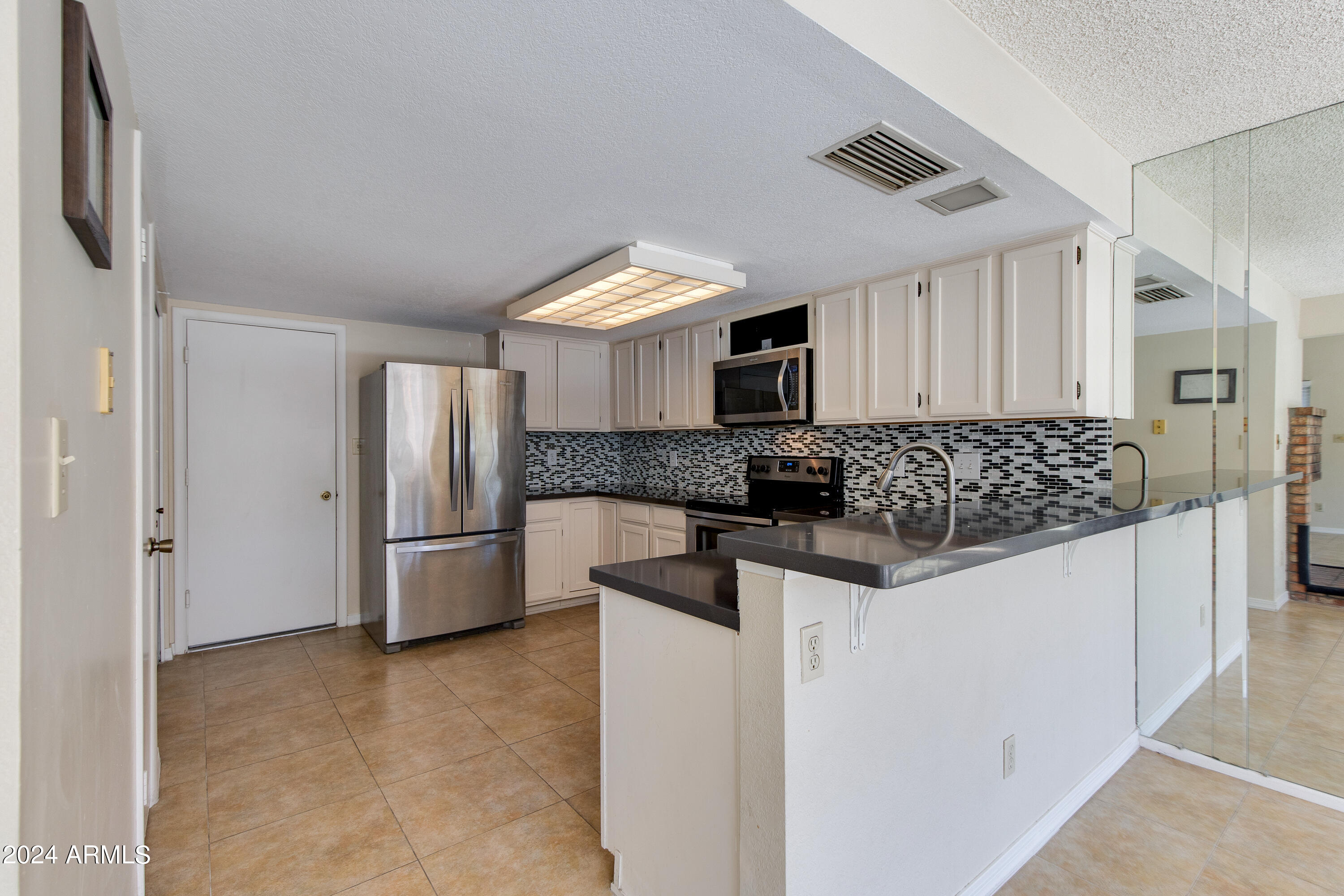 Kitchen with white cabinets, stainless steel appliances, patterned backsplash, and a dark countertop peninsula.
