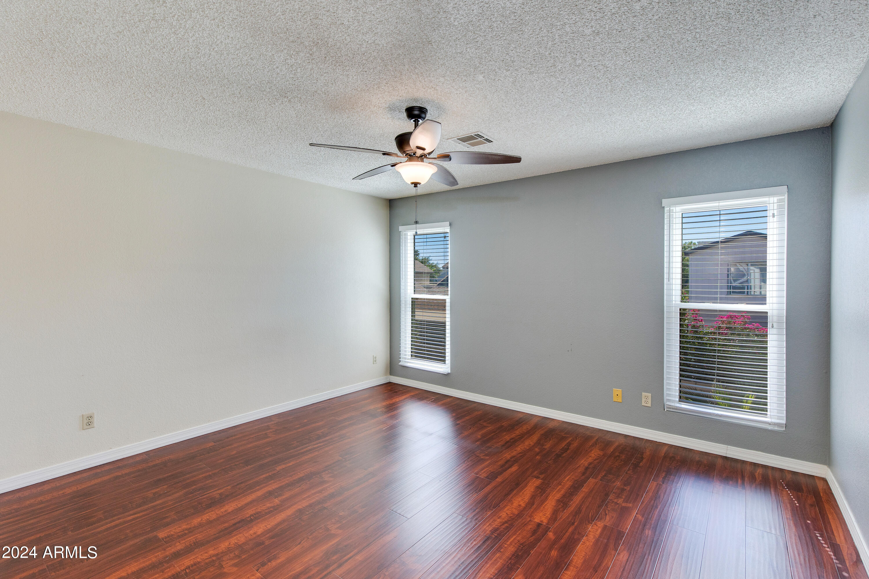 Empty bedroom with wood floors, two blinded windows, and a ceiling fan.