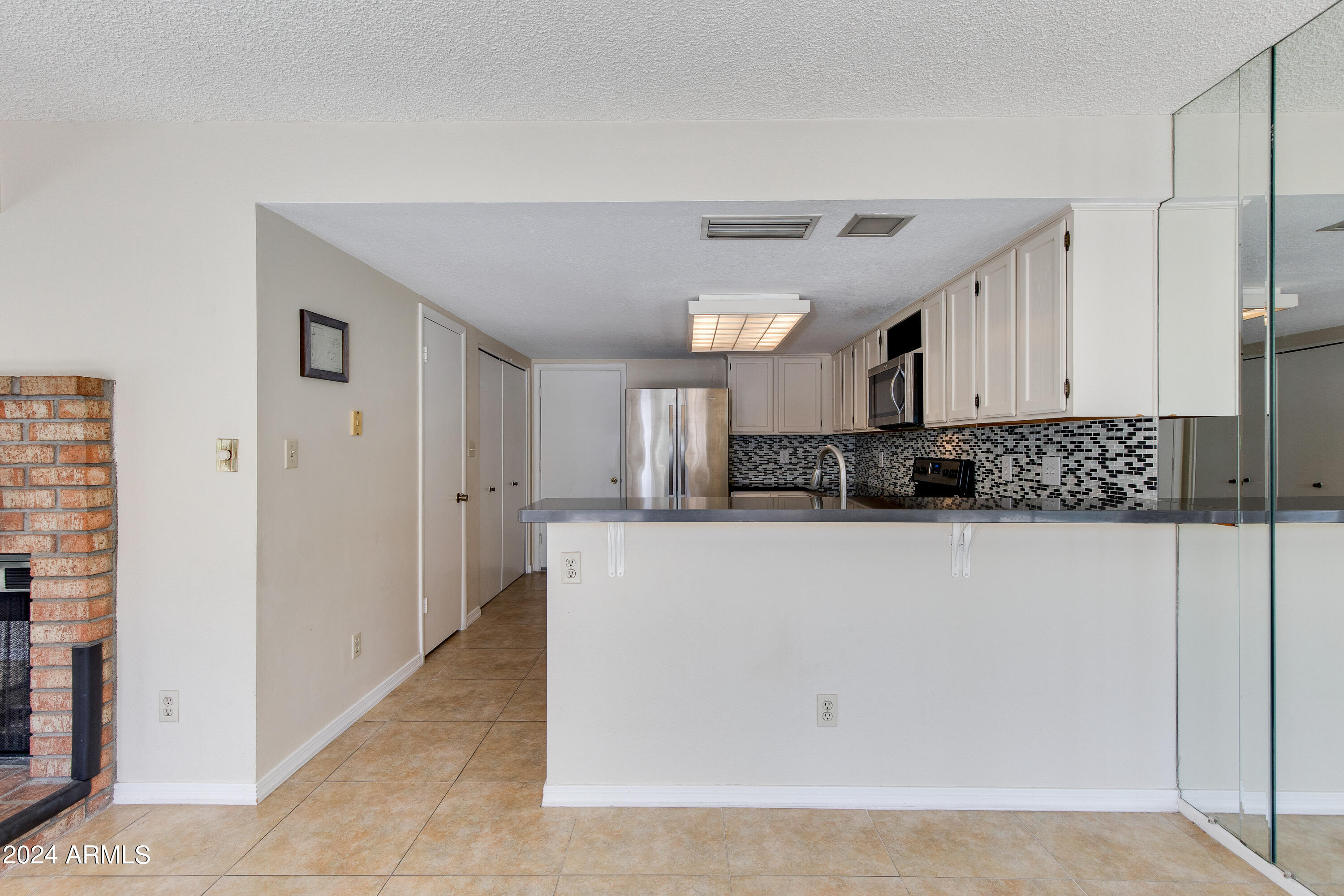 Kitchen with white cabinets, stainless appliances, mosaic backsplash, breakfast bar, and brick fireplace.