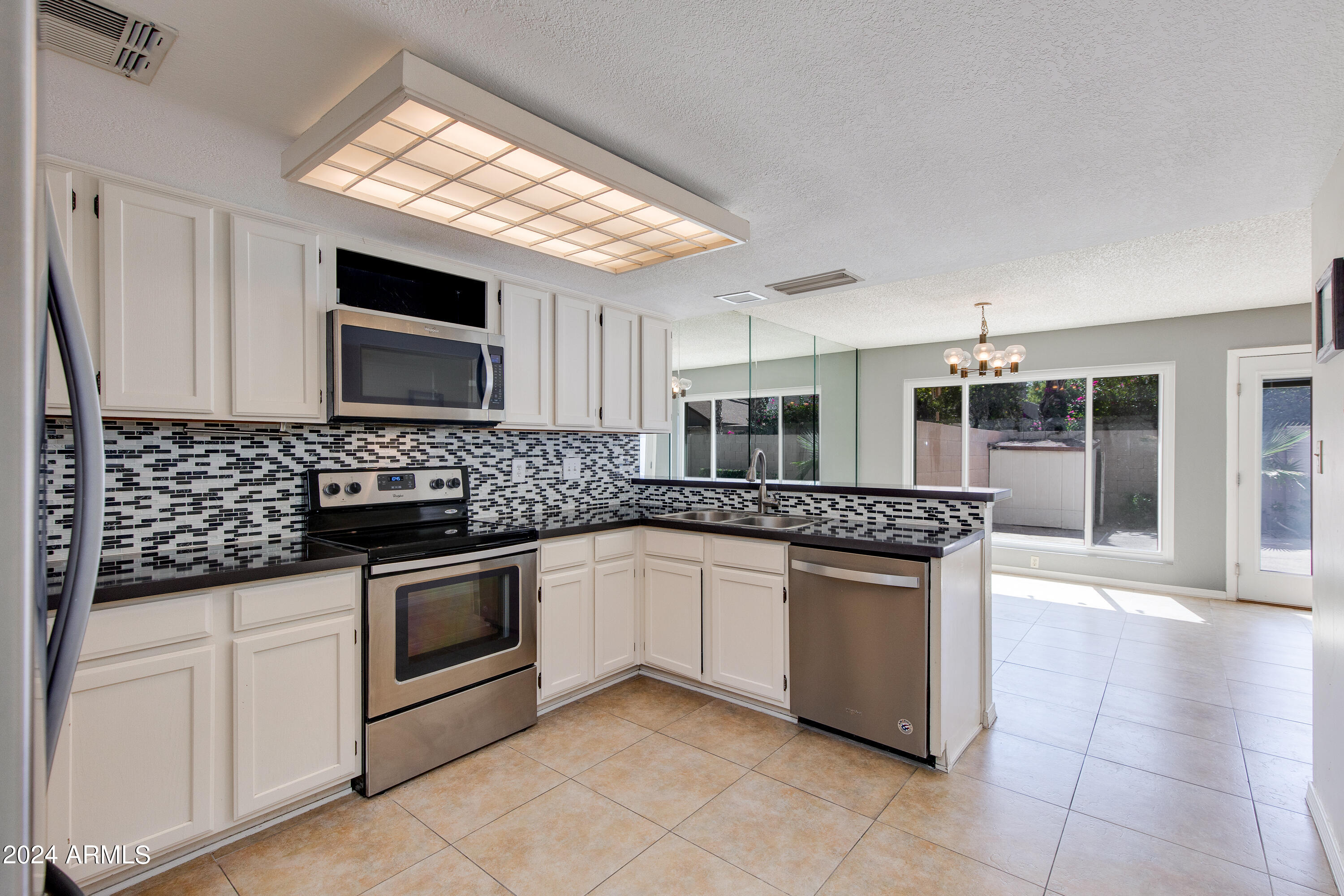 Kitchen with white cabinets, mosaic backsplash, stainless steel appliances, and a peninsula sink beside sliding glass doors.