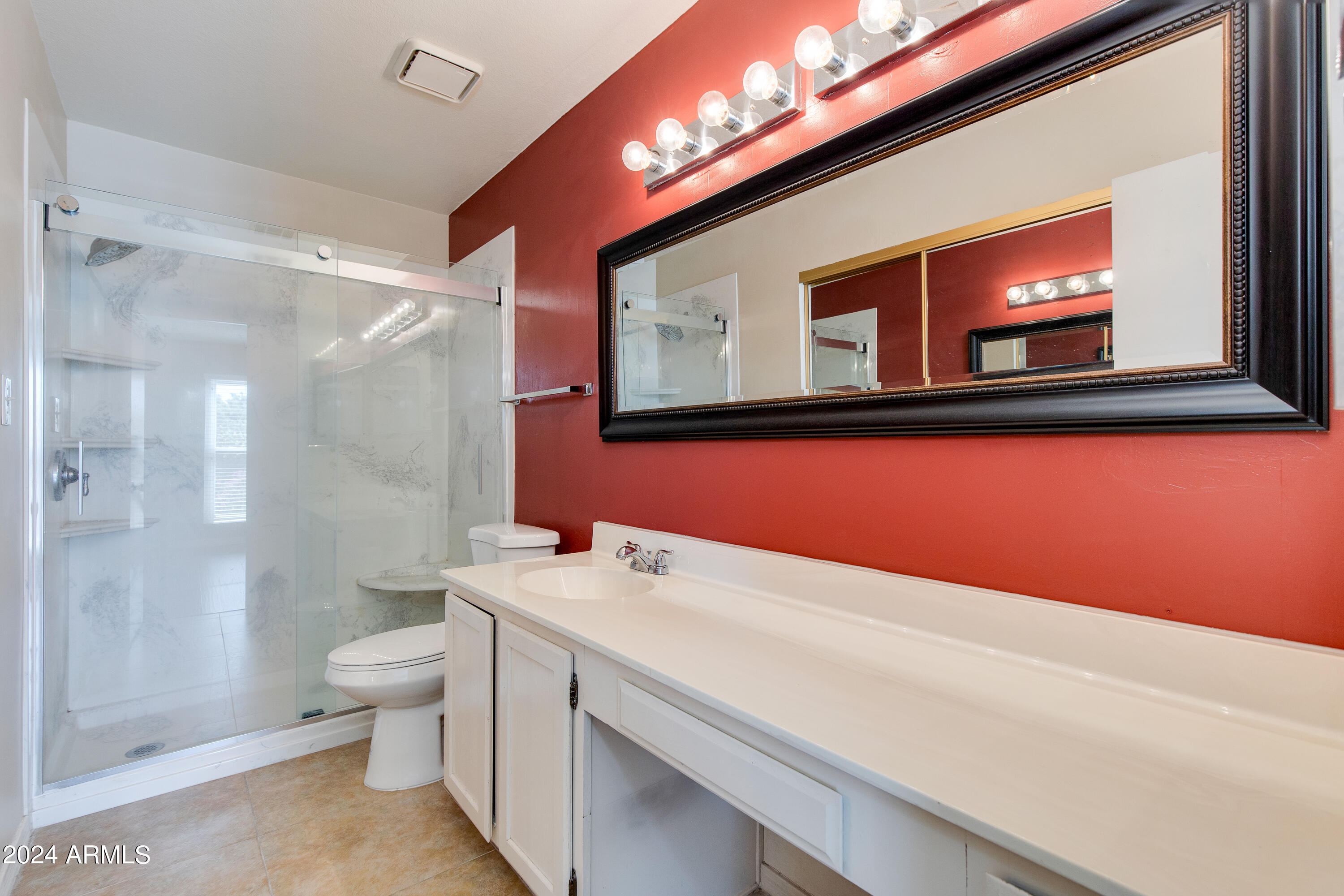 Bathroom with a long white vanity, large black-framed mirror, red wall, and glass-enclosed shower.