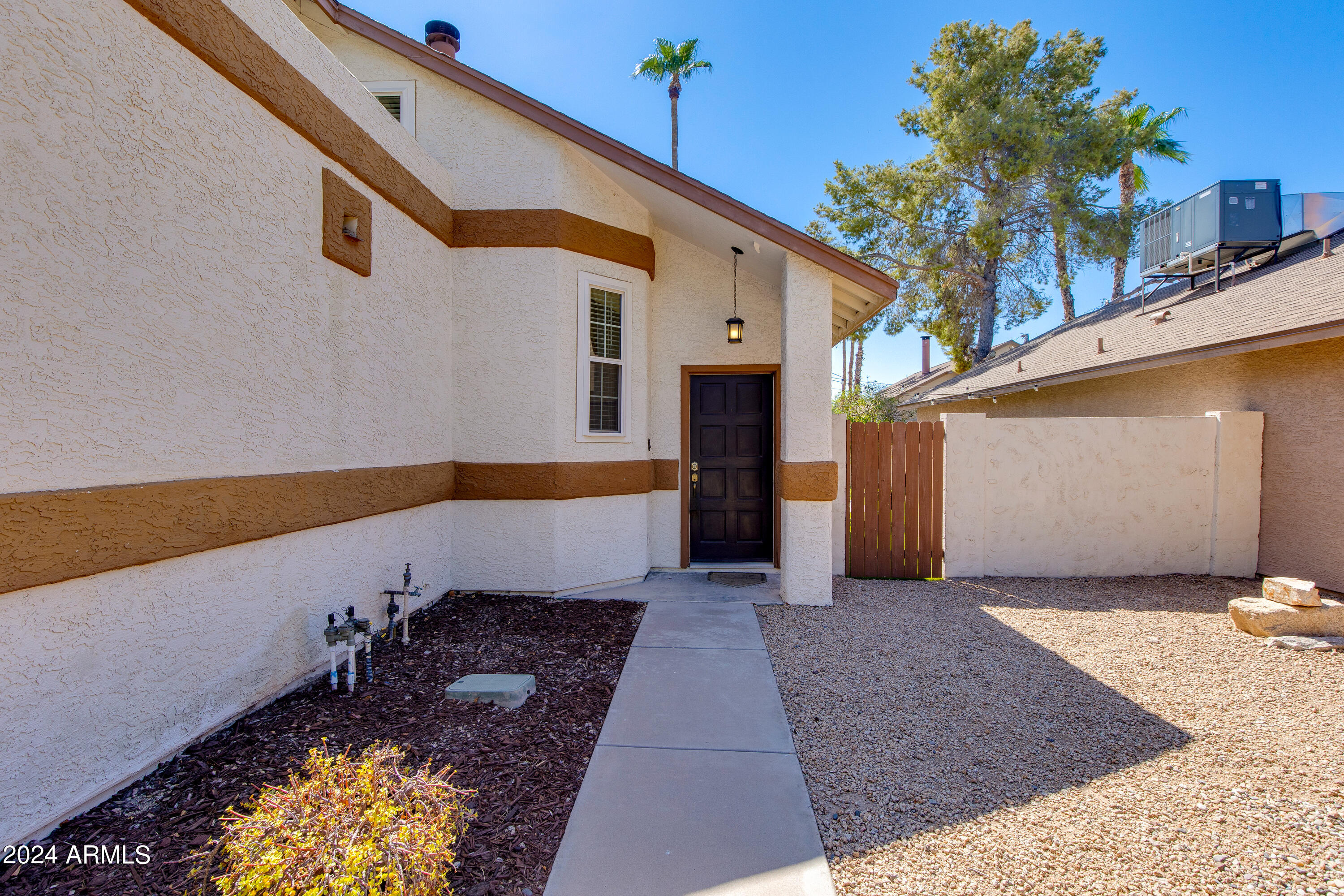 Home’s side entrance with a dark door, concrete walkway, gravel landscaping, and wooden gate.