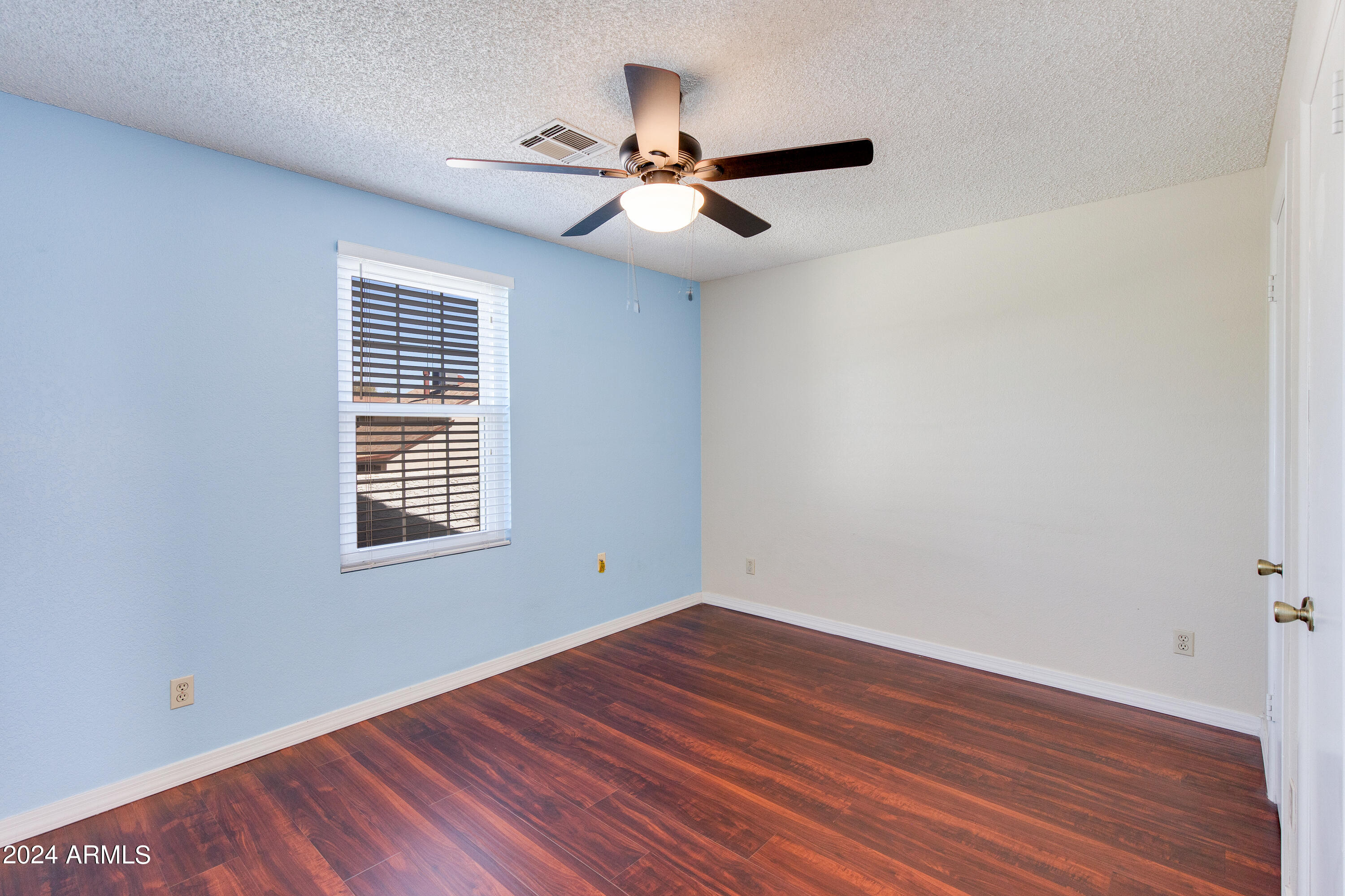 Empty bedroom with a blue accent wall, dark wood-look floors, window blinds, and ceiling fan.