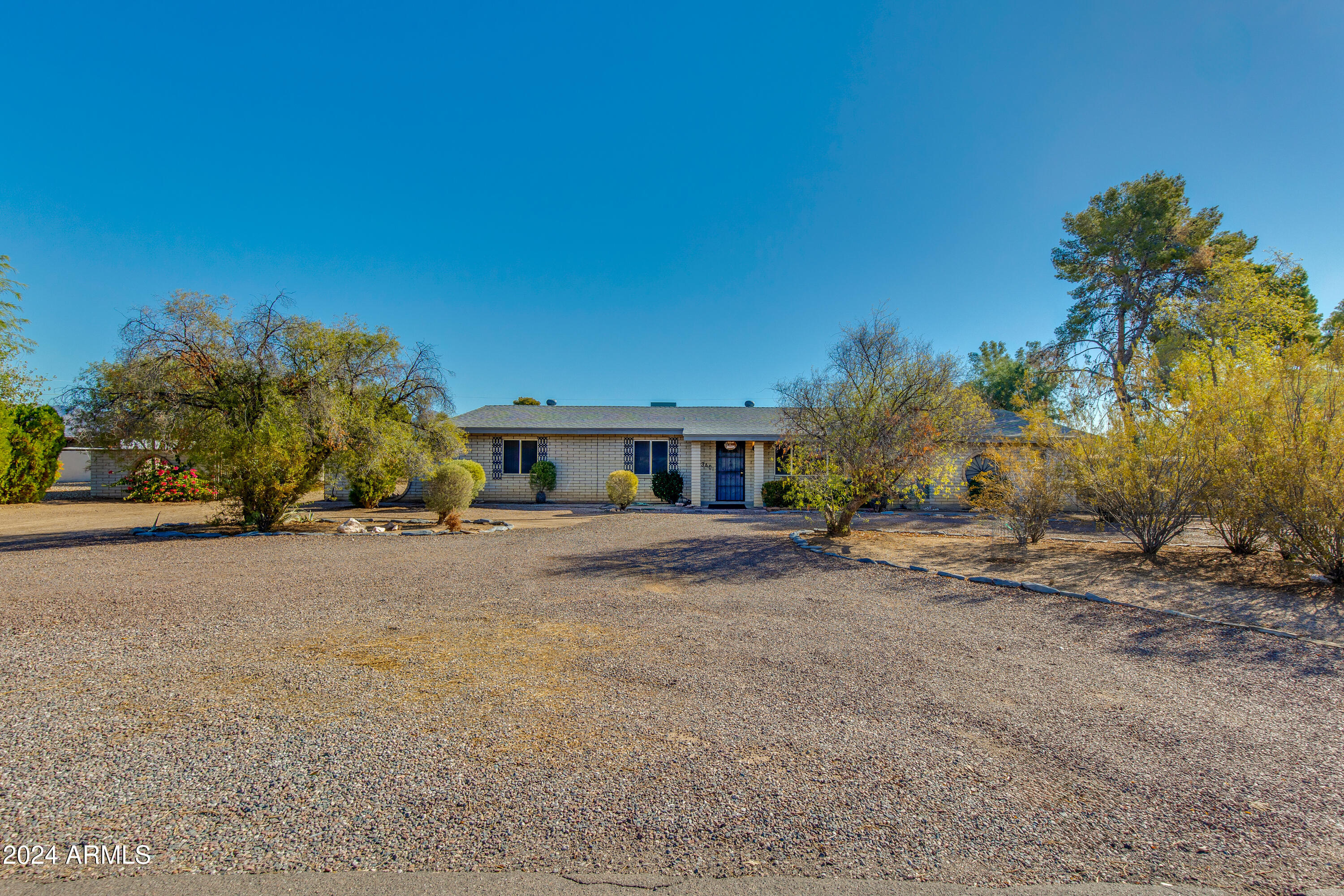 Single-story brick home with a wide gravel yard and mature trees and shrubs.