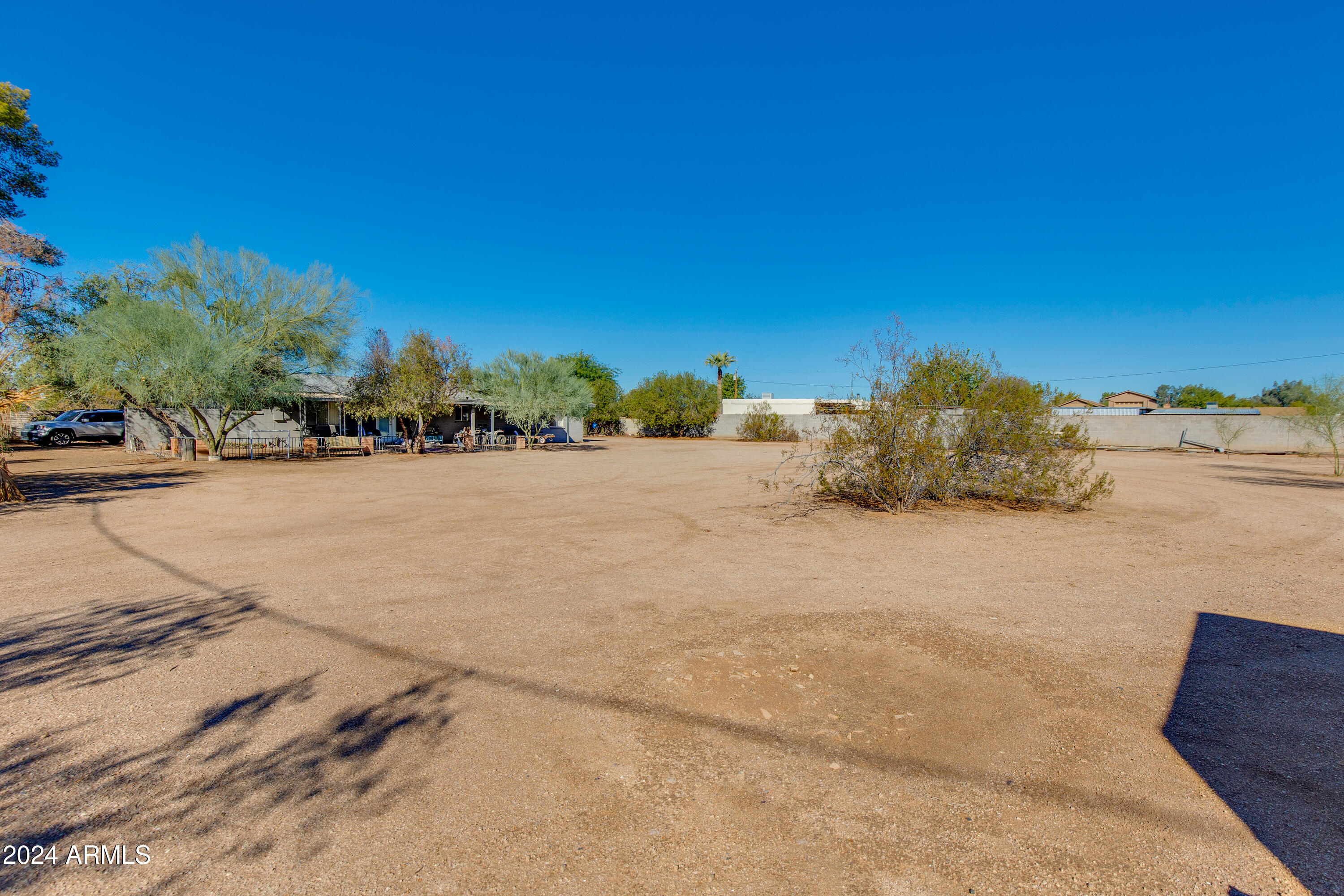 Spacious dirt yard with desert shrubs, a single-story home, and a block wall.