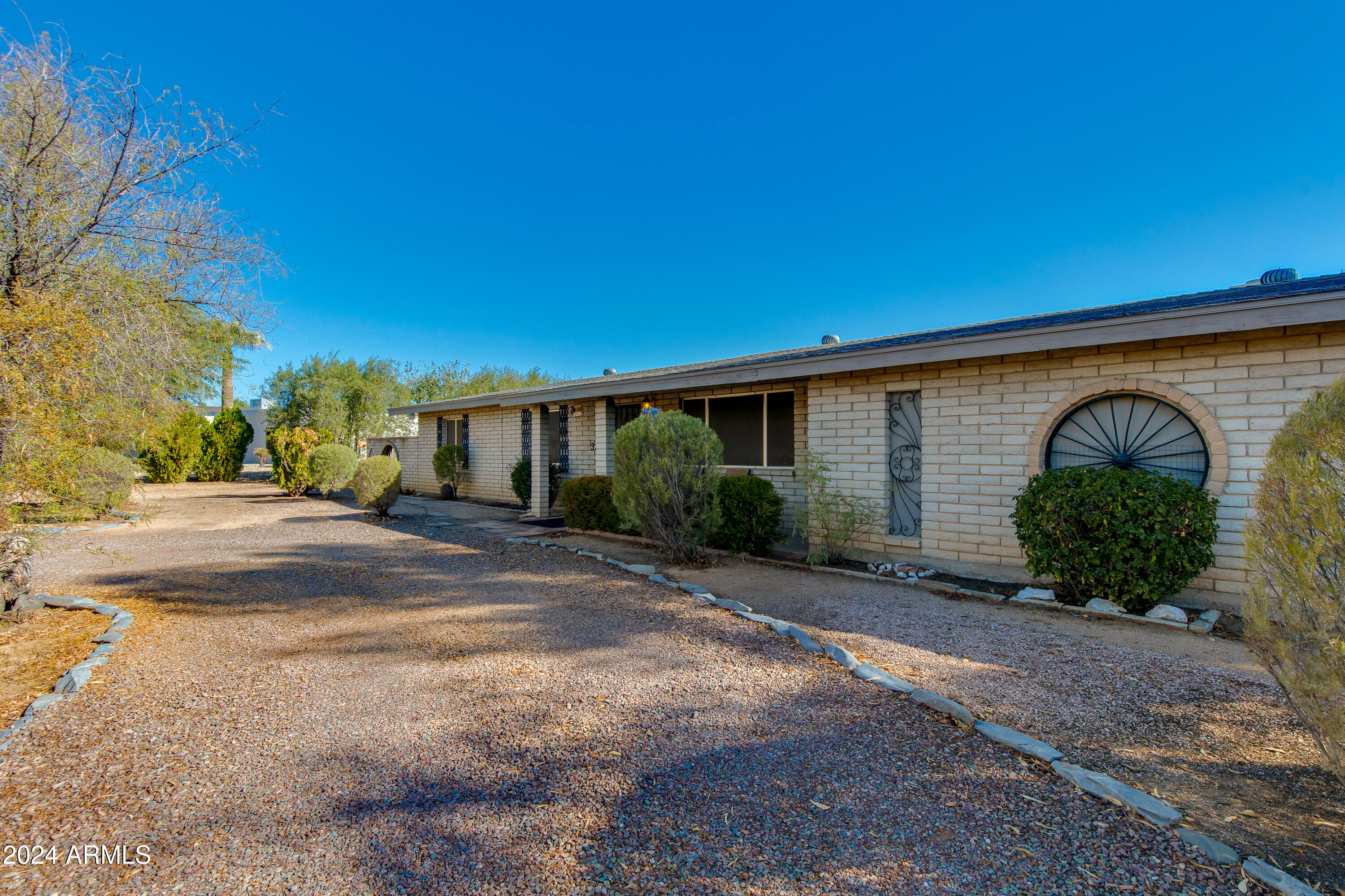 Single-story brick home with an arched window and a broad gravel front yard.