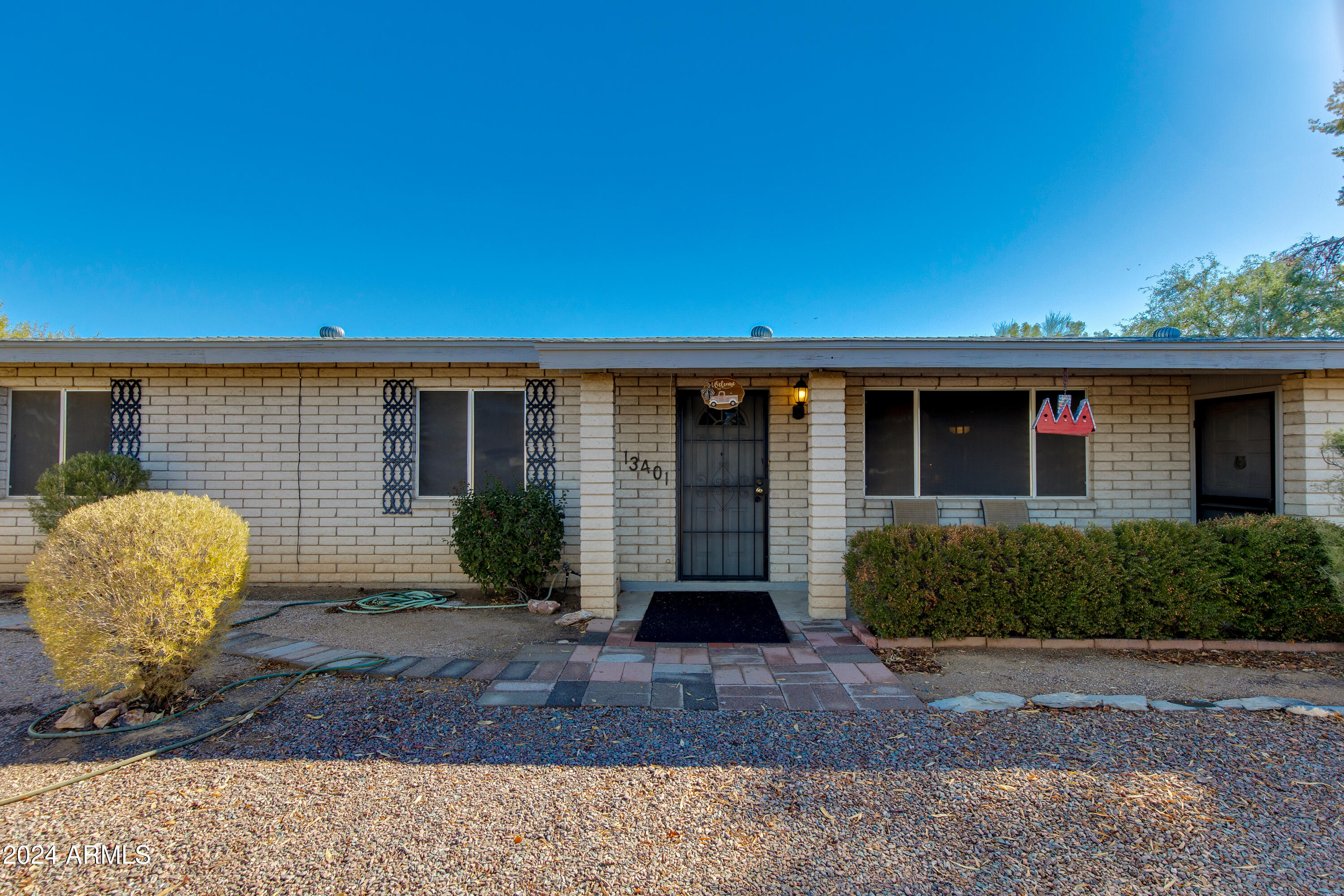 Single-story brick home with a dark metal entry door, paved walkway, and gravel landscaping.