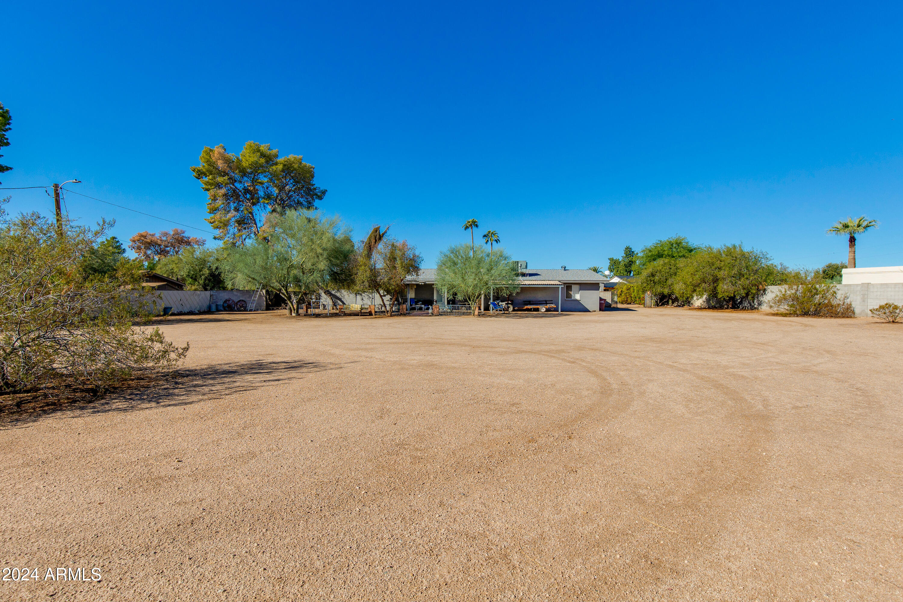 Single-story home beyond a broad gravel yard shaded by mature trees.