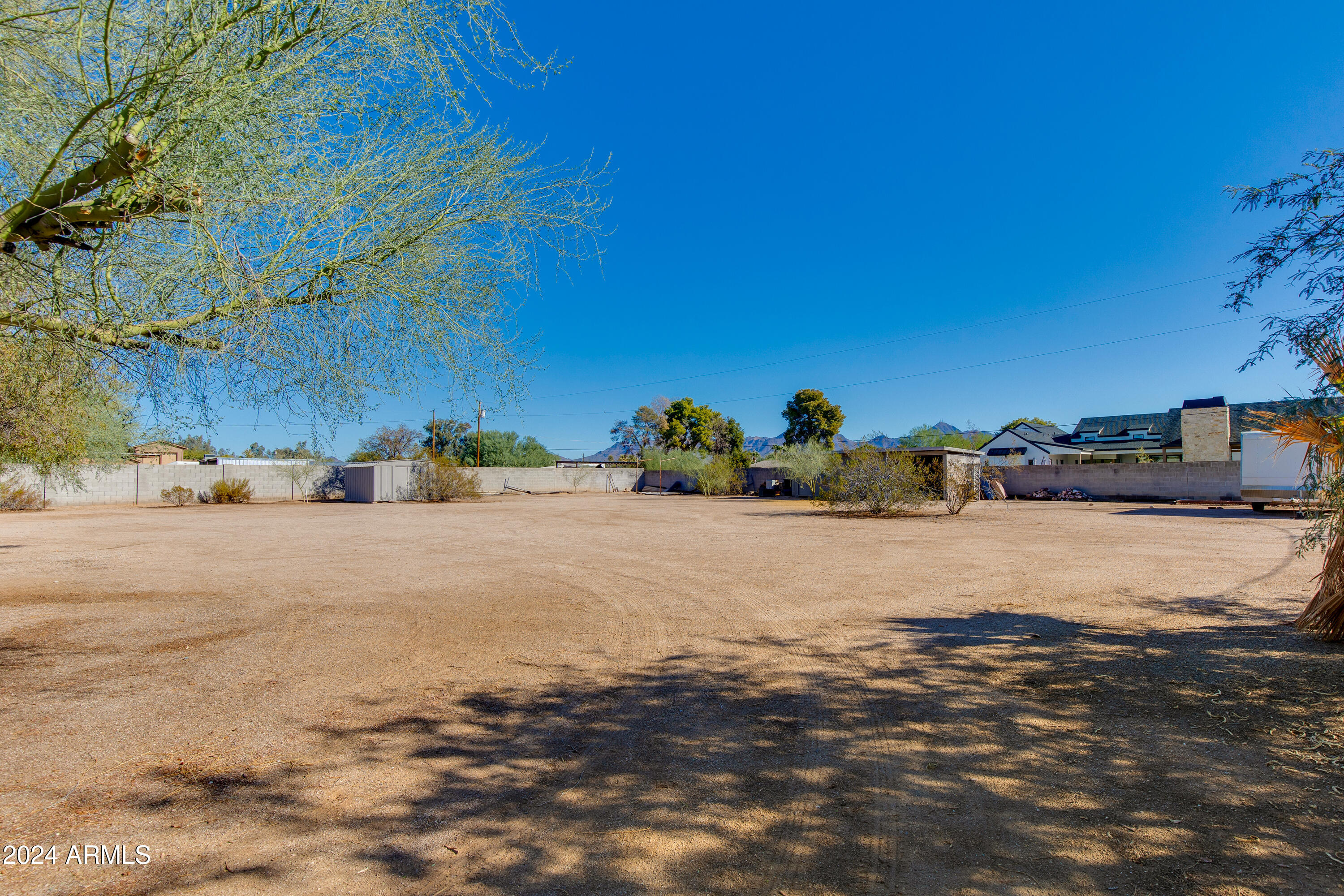 Large dirt yard enclosed by block walls, with desert trees and distant mountains.