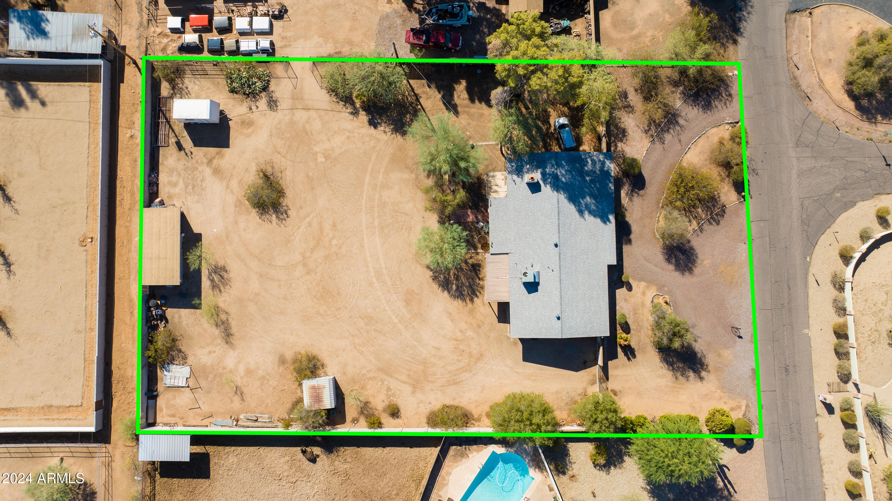 Aerial view of the property outlined in green, with a home and expansive dirt yard.