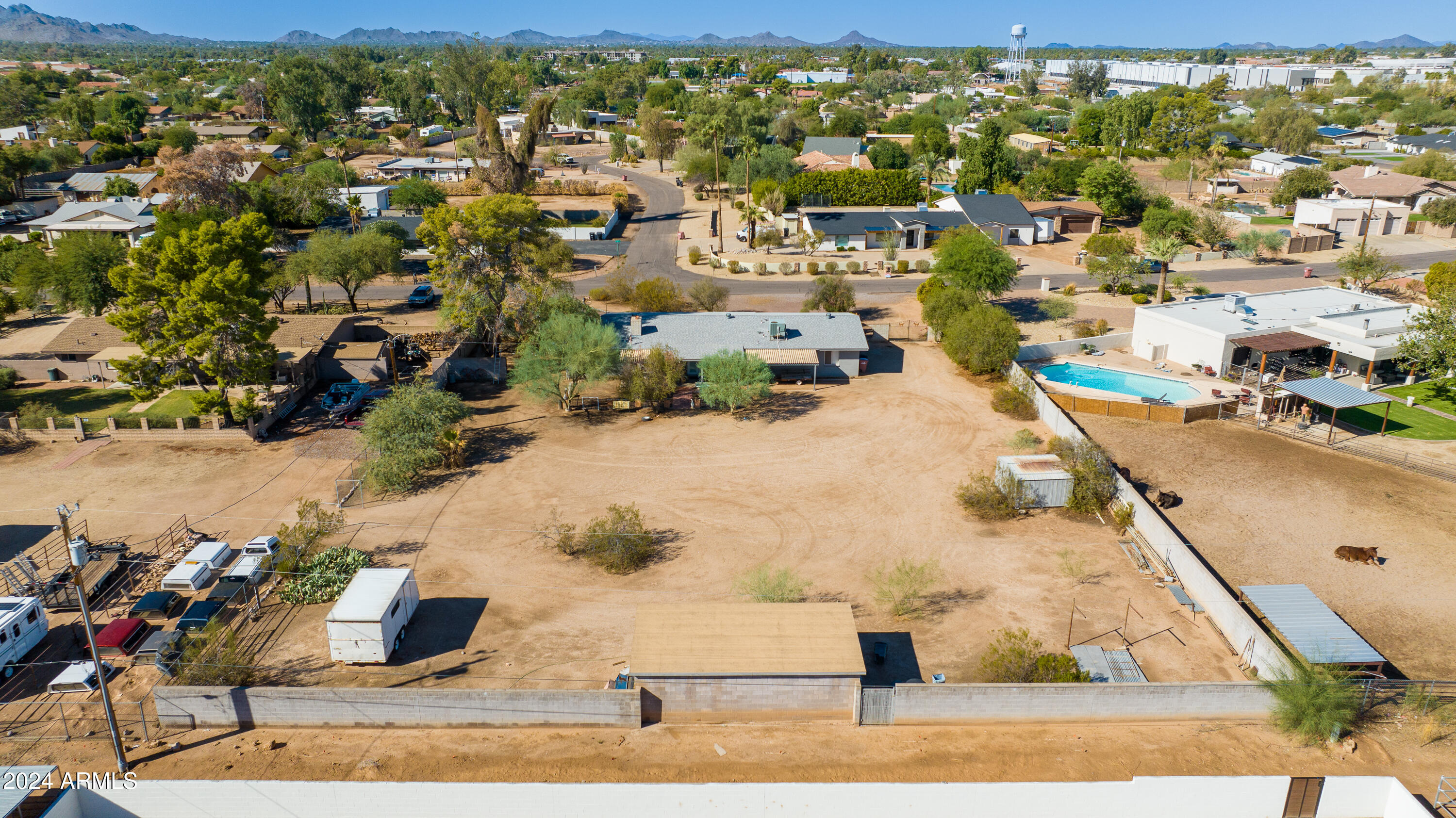 Aerial view of a walled property with a broad dirt yard, outbuildings, and mountains in the distance.