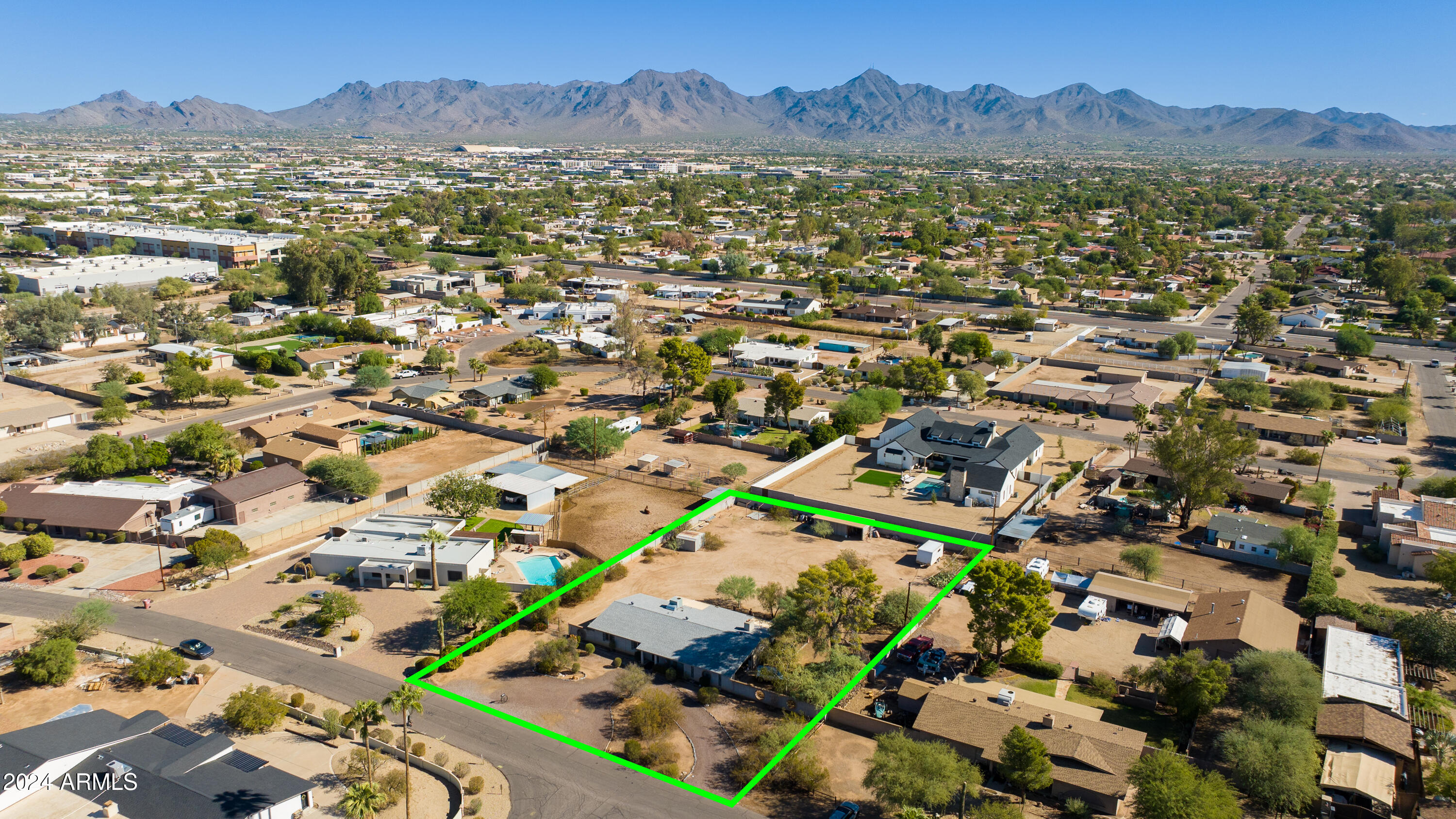 Aerial view of a home and spacious lot outlined in green, with mountains in the background.