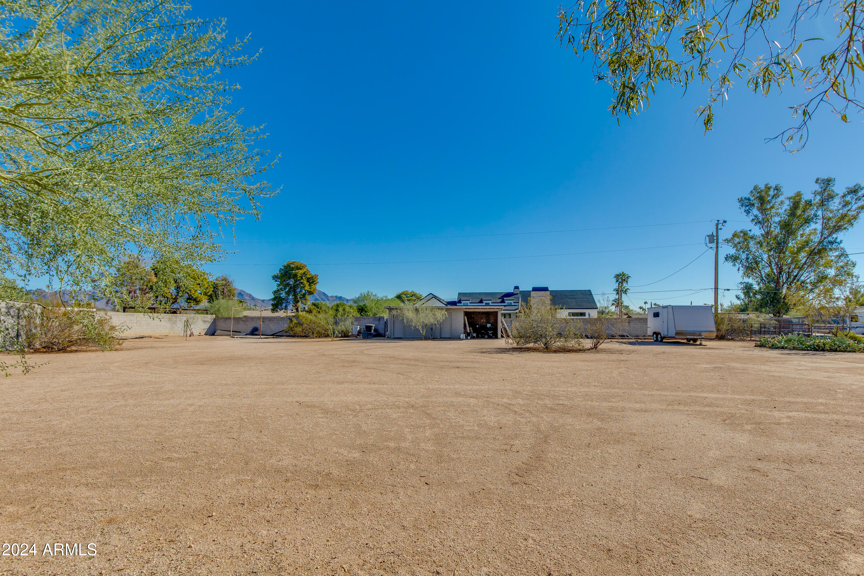 Large open yard behind a house, with an open garage, a parked trailer, and distant mountains.