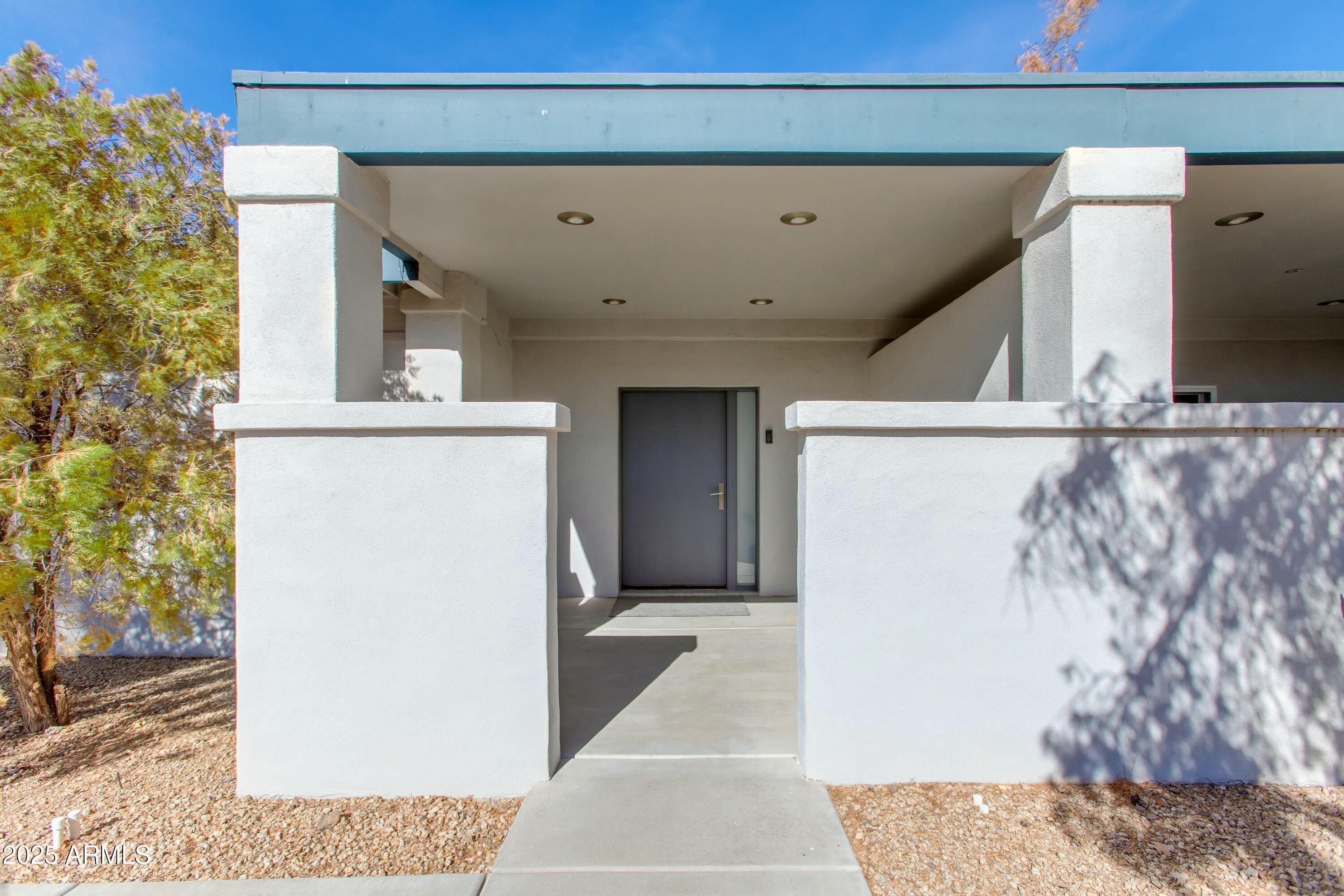 Modern home entrance with a covered porch, square stucco columns, and a gray front door.