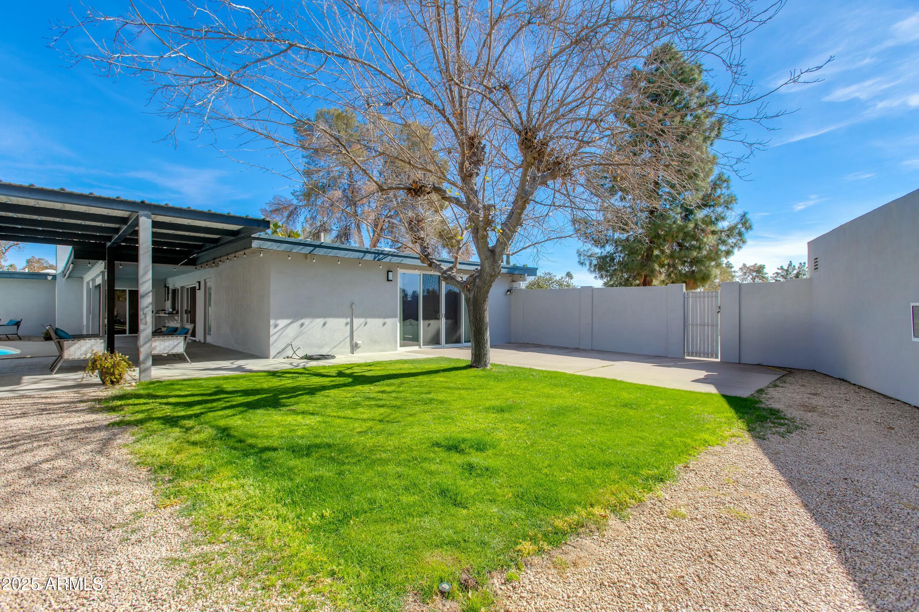 Backyard with a broad green lawn, mature tree, and covered patio beside the home.