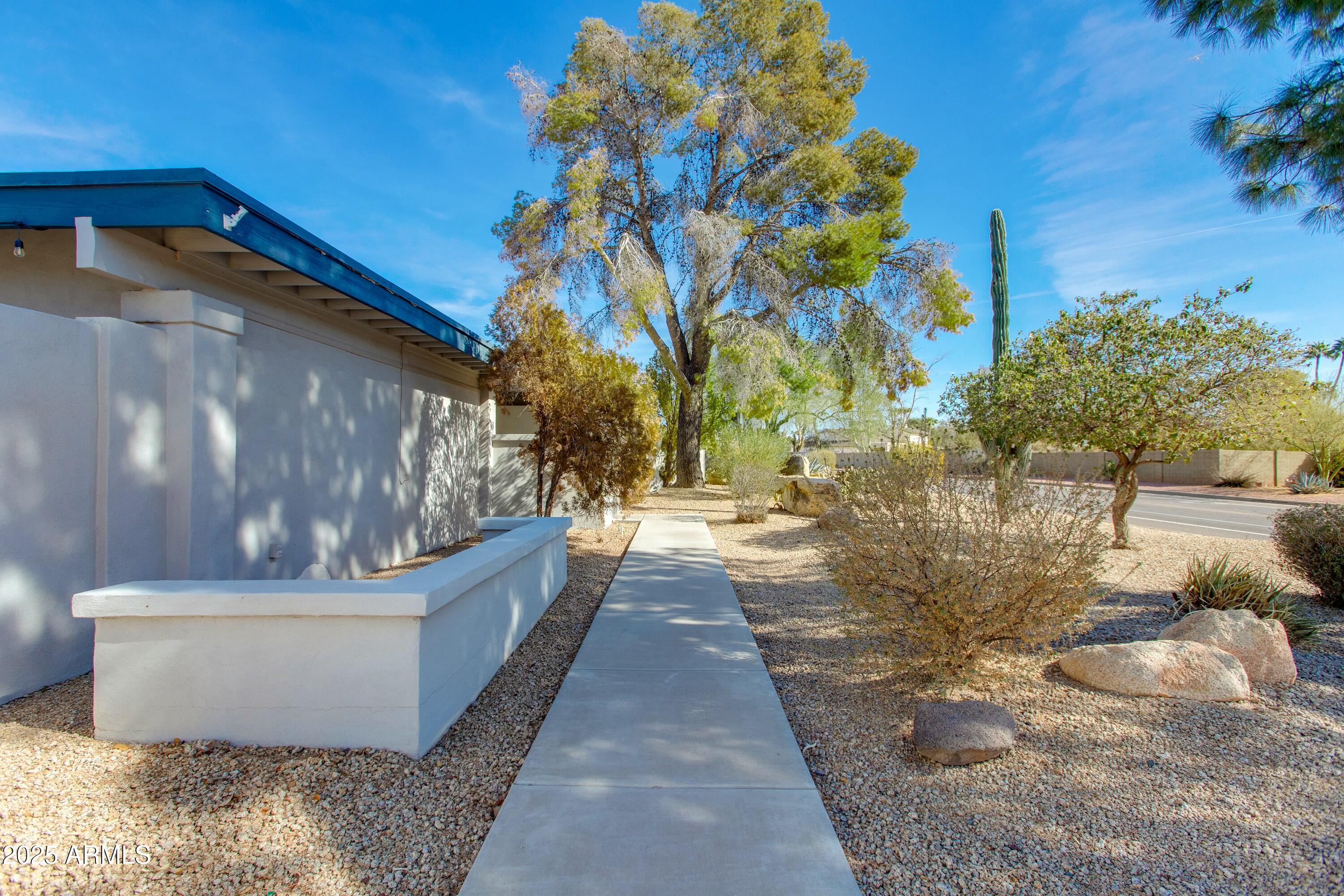 Home exterior beside a concrete walkway through gravel landscaping with desert plants and a tall saguaro.