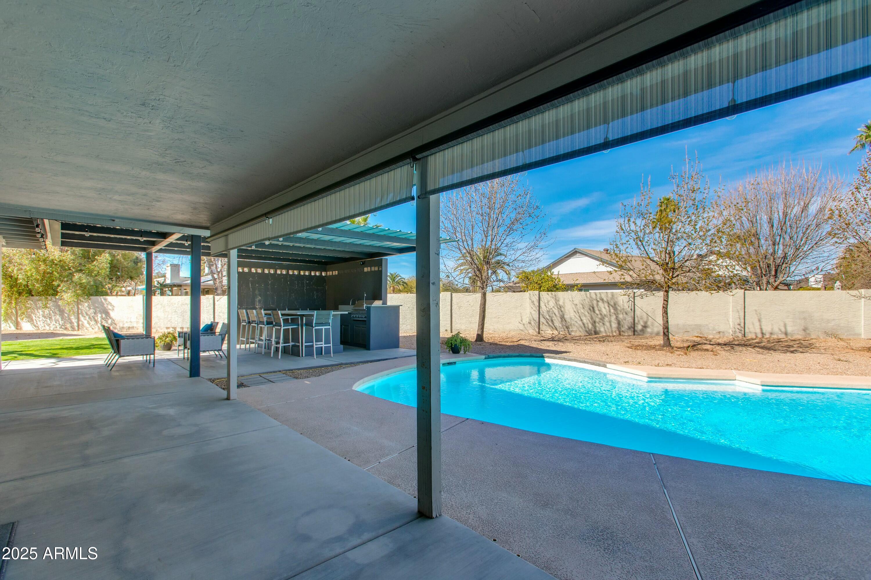Backyard pool beside a covered patio with an outdoor kitchen and bar seating.